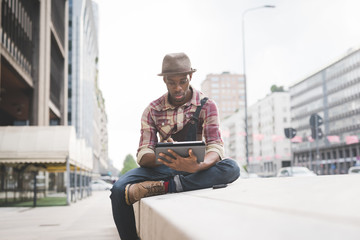 Fototapeta na wymiar Young handsome afro black man outdoor in the city sitting using tablet - technology, social network, communication concept