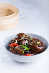 Braised pork hocks in a shallow bowl. White background , a steamer basket in the background