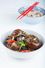 Braised pork hocks in a shallow bowl. White background , a bowl with rice in the background