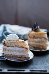 a beautiful delicious cake and the pieces in twoo white saucers beige yellow on cutting Board on dark black background close-up