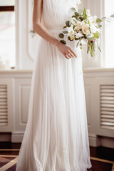 Fototapeta premium beautiful wedding bouquet of green flowers, white roses in the hands of the bride dress
