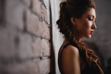 beautiful girl with bright makeup wearing a black dress with pigtails looking down on a light brick background closeup