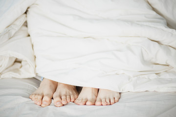 the legs of two lovers men and women girl and boy stick pop out under the white soft fluffy clean blanket on the bed the foreground white background