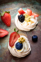 Mini Pavlova meringue cakes with berries and passion fruits on rustic vintage background. Top view.