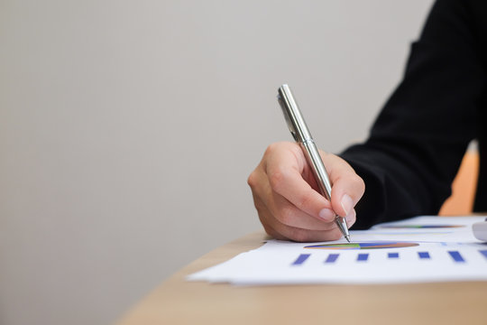 close up businesswoman hand using pen for writing data information on financial paperwork concept.