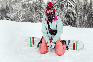 Fototapeta na wymiar Lady in blue ski jacket and pink pans poses on her snowboard on the hill