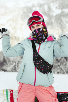 Woman in blue ski jacket raises her hands up posing on snowboard