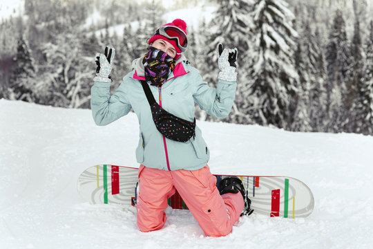 Warm dressed woman in ski suit poses on the knees in winter forest
