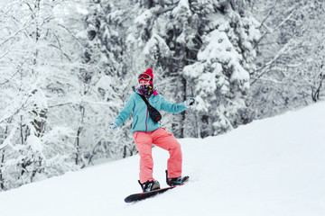 Fototapeta na wymiar Woman in blue ski jacket and pink pants stands on the snowboard somewhere in winter forest