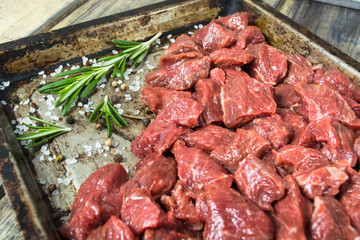 Raw meat with salt, pepper and rosemary on the baking pan