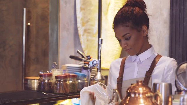 Smiling Dark-skinned waitress standing on bar and wipes wineglass