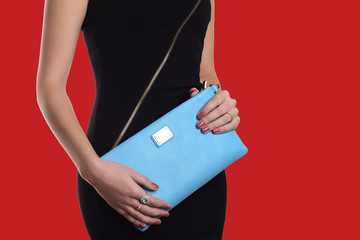 The fashionable young woman in black dress holding blue clutch. Red background