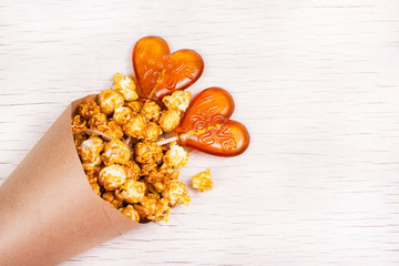 Golden Caramel popcorn in a paper cup and lollipops in the shape of a heart. Copy space.