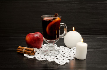 Mulled wine with spices on a lace napkin. White candles, cinnamon sticks and apple. Black wood...