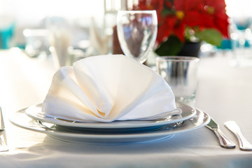 Linen napkin on a plate on the table covered with a white tablecloth.