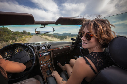 Two Young Women In Convertible Car, Driving Along Scenic Road, Rear View