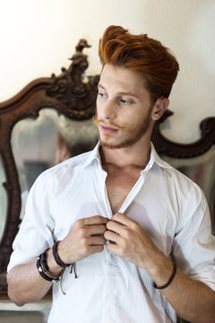 Young man with red hair, buttoning shirt