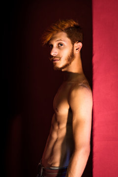 Portrait of young man with red hair, leaning against red wall
