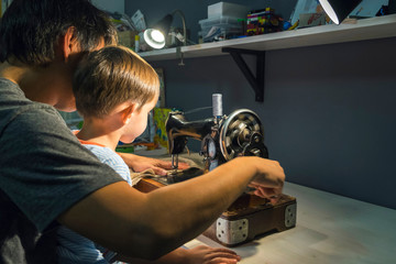 Over shoulder view of boy with father learning to turn sewing machine handle