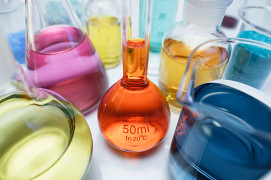 Volumetric flask containing solution of potassium dichromate (VI) (K2Cr2O7) and other flasks of transition metal salts, dry chemicals and solutions. Compounds with transition metals are often colored