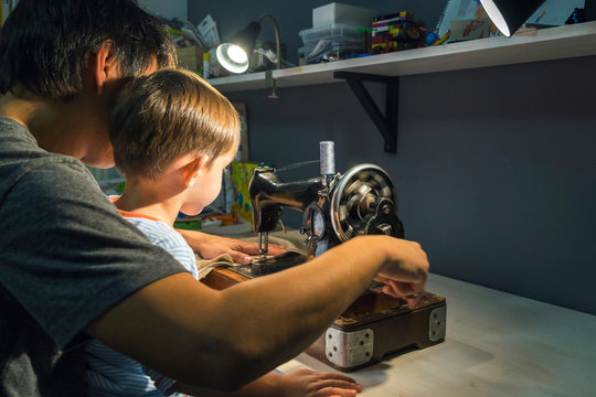 Over shoulder view of boy with father learning to turn sewing machine handle