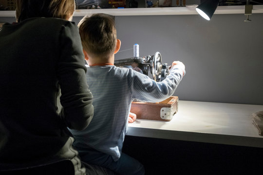 Rear view of boy with mother learning to turn sewing machine handle