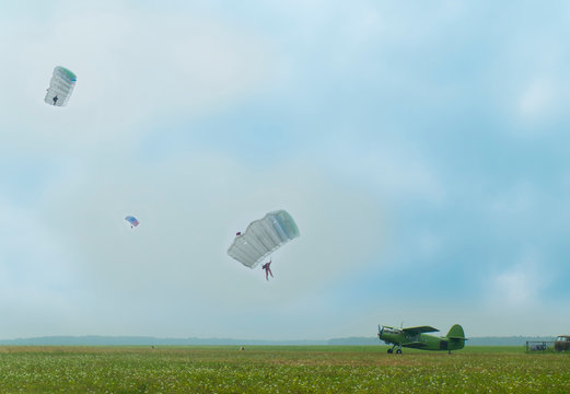 Distant view of three people parachuting down to airfield with a vintage aircraft