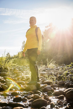 Female hiker gazing from sunlit riverbed in Englishman River Falls Provincial Park , Vancouver Island, British Columbia, Canada