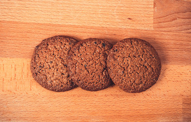 Homemade oat cookies on a wooden background. Oatmeal cookies on a old wooden cutting board. Freshly baked oatmeal raisin cookies on rustic wood table. Closeup from above with natural lighting.