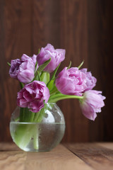 Violet tulips in a round vase on a wooden background