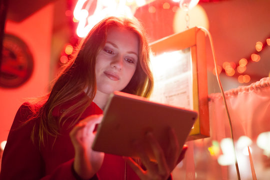 Young woman using digital tablet in neon signage shop, London, UK