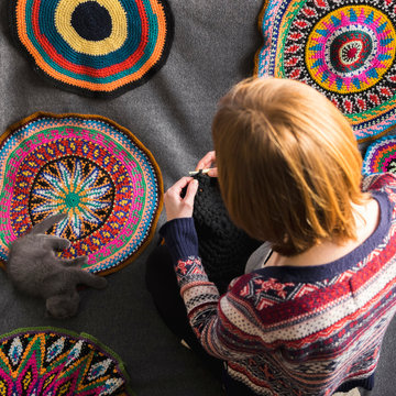 Overhead view of woman sitting on floor crocheting, surrounded by crochet circles