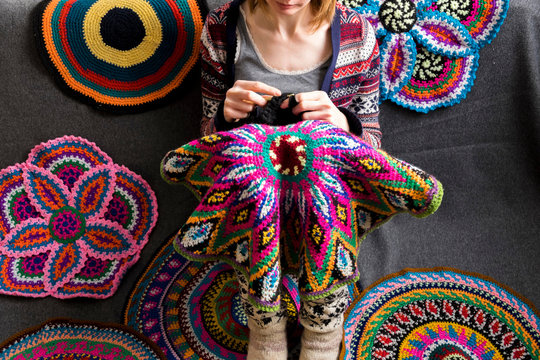 Cropped view of woman sitting on floor crocheting, surrounded by crochet circles