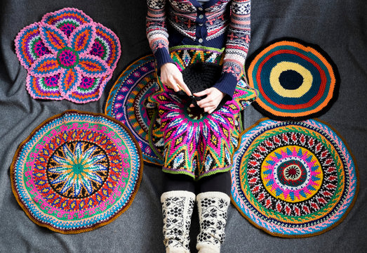 Neck down view of woman sitting on floor crocheting, surrounded by crochet circles