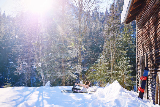 Woman practicing bow yoga pose by log cabin in snow,  Austria