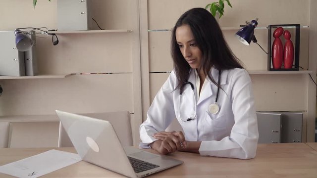 woman md has conference call with colleagues or remote meeting. Mixed race physician sitting at the office use laptop talking and smiling.