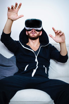 Mid adult man on sofa with arms raised watching virtual reality headset