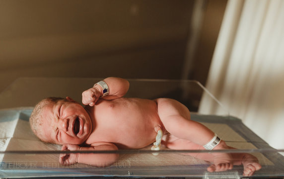 Naked crying newborn baby girl lying on hospital weight scales