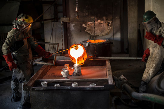 Metalworkers working in foundry, pouring molten bronze