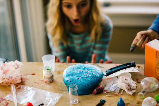 Girls doing science experiment, surprised by blue liquid foaming in frying pan