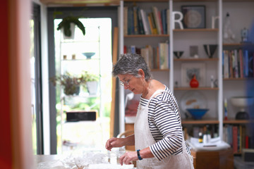 Senior woman in kitchen, arranging clear pots on work surface