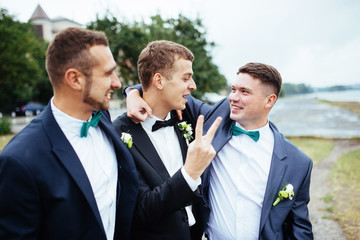 Confident smiling handsome groom in black suit with two groomsma
