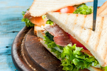 Club sandwiches with fresh lettuce, tomato, cucumber and salmon (trout). On crunchy toast. On blue rustic table, picnic, close view copy space