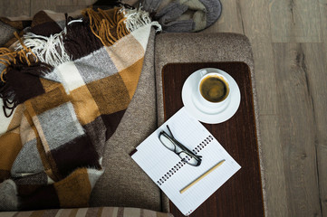 Cup of coffee Notepad glasses and a telephone. On the sofa lay a blanket and Slippers.
