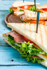 Club sandwiches with fresh lettuce, tomato, cucumber and salmon (trout). On crunchy toast. On blue rustic table, picnic, close view copy space