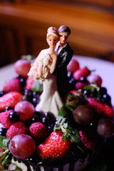 naked tiered cake with fruits and berries, and with figures of the bride and groom