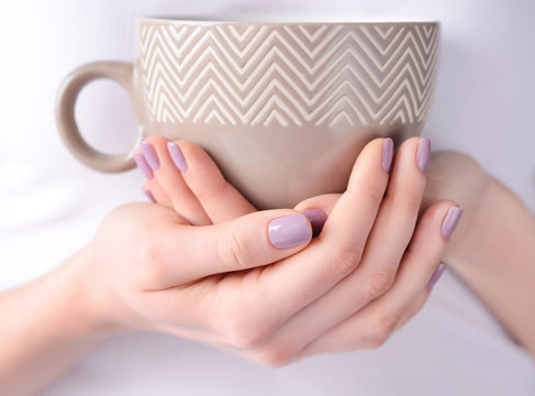 Hands of a young woman with pink manicure holding a cup of tea