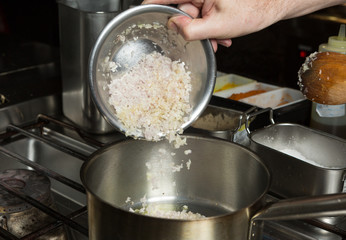 Minced garlic and finely sliced onion being dropped into a metal frying pan of olive oil. Step by step recipe cooking.