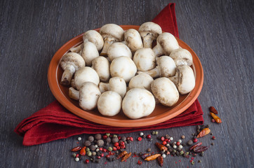 Fresh mushrooms with spices on plate, wooden background