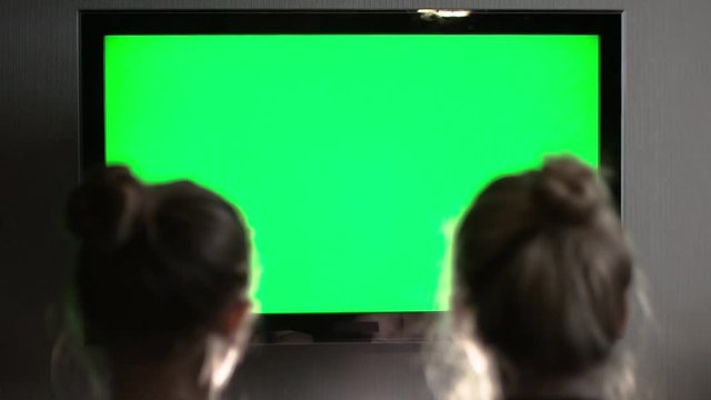 Two young long-haired blond watching green TV screen and tilt their heads to one another